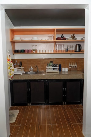 Una cucina compatta con mobili in legno, un piano di lavoro e mensole piene di stoviglie e utensili da cucina.