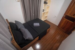 Una camera da letto piccola e ordinata, con un letto, un armadio in legno, uno scaffale con oggetti e una tenda.