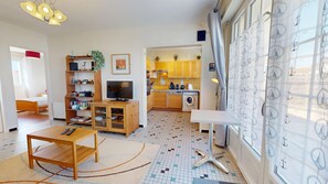 A compact living space with a TV, wooden furniture, a washing machine, and a kitchen area. - Le Porte Bonheur (Saint-Hilaire-de-Riez)