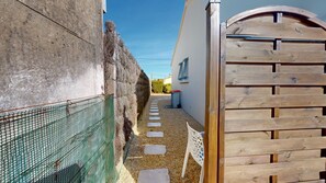 A narrow pathway with a wooden gate, a gravel path, and a green mesh fence. - Le Porte Bonheur (Saint-Hilaire-de-Riez)