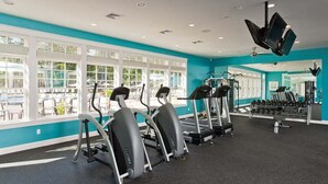 Ein Fitnessstudio mit Laufbändern, Crosstrainern und Kraftgeräten, großen Fenstern und einer türkisblauen Farbgestaltung.
