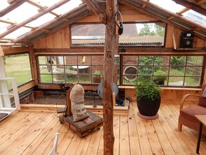A wooden structure with a sloped roof, large windows, a wooden bench, a table, and a potted plant.