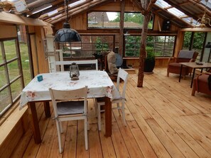 Eine Holzterrasse mit Tisch und Stühlen, einem hängenden Laternen und Blick ins Freie durch große Fenster.