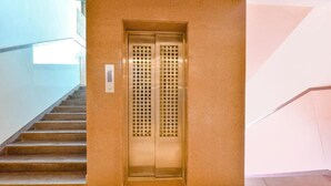 An elevator with a control panel, located next to a staircase with a glass railing. - Hotel PVR (Ahmedabad)