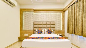 A modern hotel room with a large bed, a headboard with a geometric pattern, and a wooden accent wall. - Hotel PVR (Ahmedabad)