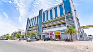 A multi-story building with a modern design, featuring a prominent entrance and a parking area with several cars and motorcycles. - Hotel PVR (Ahmedabad)