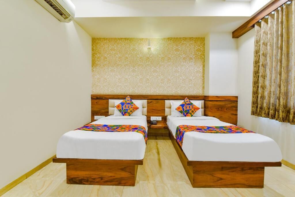 A hotel room with two beds, a wooden headboard, a patterned wall, and a curtain.