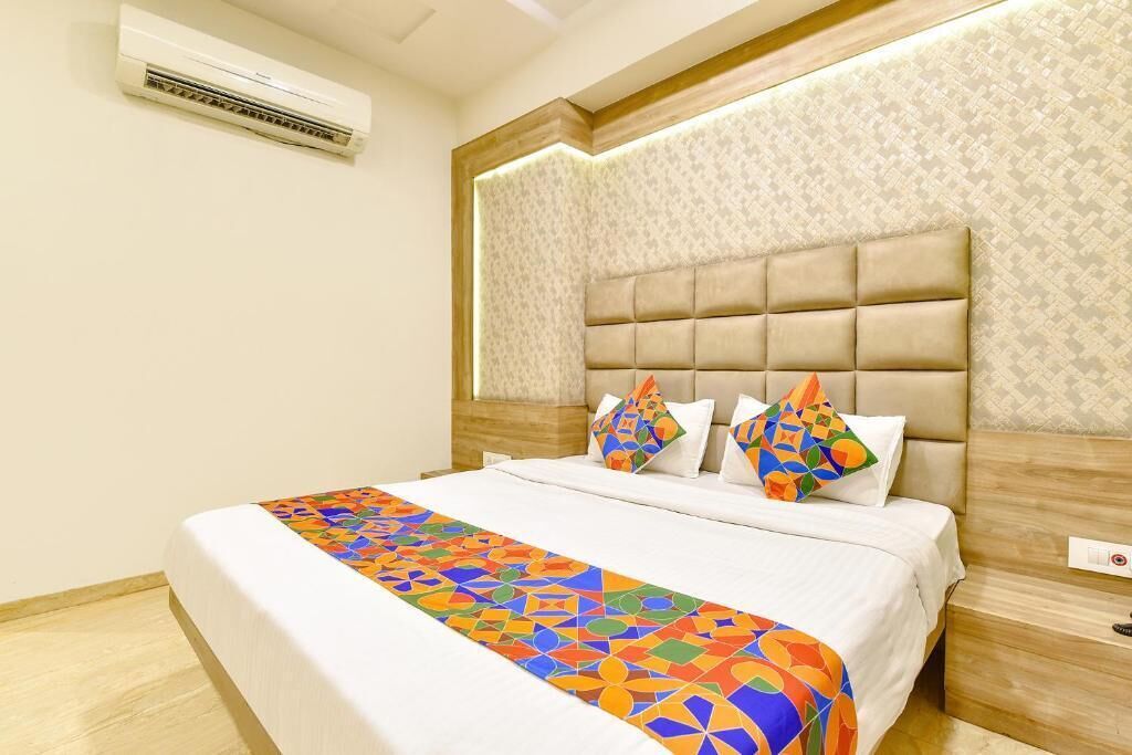 A hotel room with a bed, a headboard, a patterned wall, and an air conditioning unit.