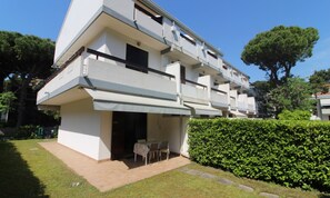 A modern multi-story residential building with a flat roof, a covered outdoor seating area, and a well-maintained garden. - Relaxing villa with fenced garden (Lignano Sabbiadoro)