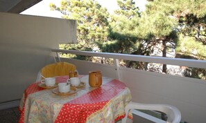 Un balcón con una mesa dispuesta para dos personas, con mantel floreado y una silla amarilla.