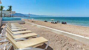 A beach with sun loungers, umbrellas, and a pool area. - Amazing Studio with Oceanview - Pool - Beach - Gym (Puerto Vallarta)