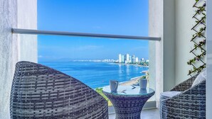 A balcony with wicker furniture, a glass table, and a view of a coastal cityscape. - Amazing Studio with Oceanview - Pool - Beach - Gym (Puerto Vallarta)