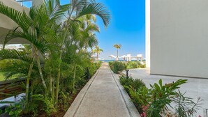 A pathway lined with tropical plants leading to a pool area with umbrellas and lounge chairs. - Amazing Studio with Oceanview - Pool - Beach - Gym (Puerto Vallarta)