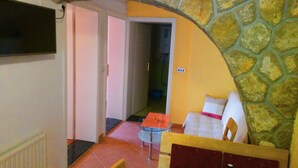 Ein Wohnzimmer mit einer Steinwand, einem weißen Sofa, einem Glastisch und einem an der Wand befestigten Fernseher.