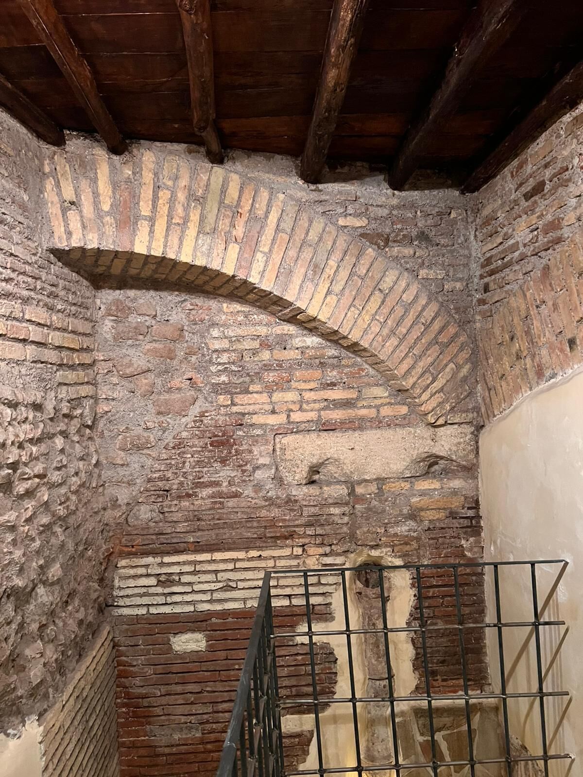 An arched brick ceiling with exposed beams and a metal railing in a rustic interior.