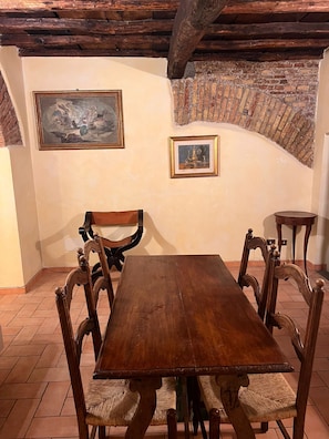Ein rustikaler Essbereich mit Holztisch und -stühlen, zwei gerahmten Bildern an der Wand und freiliegenden Backsteinwänden.
