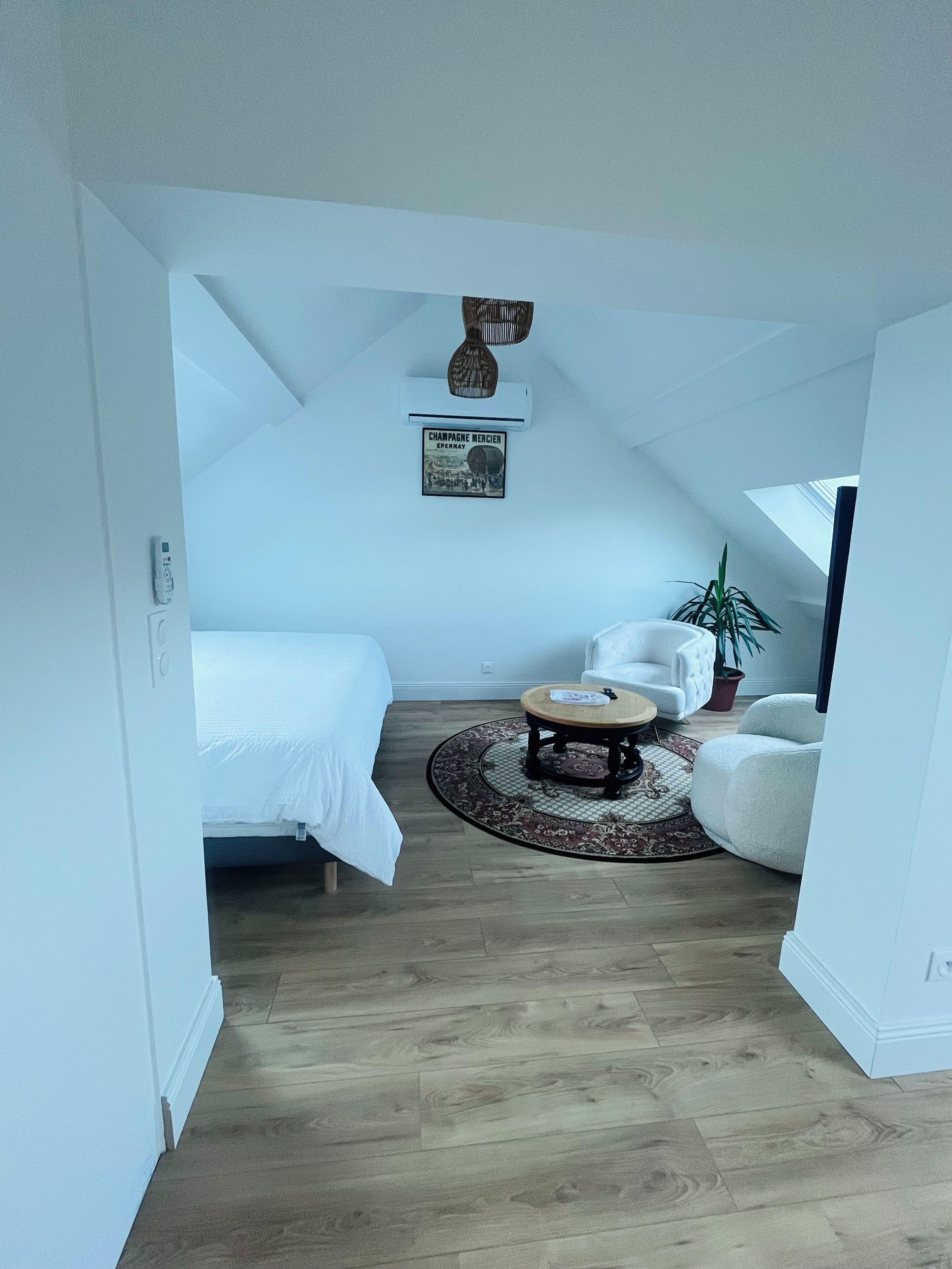 Un dormitorio con una cama, un sillón blanco, una mesa redonda de madera y una planta en maceta.