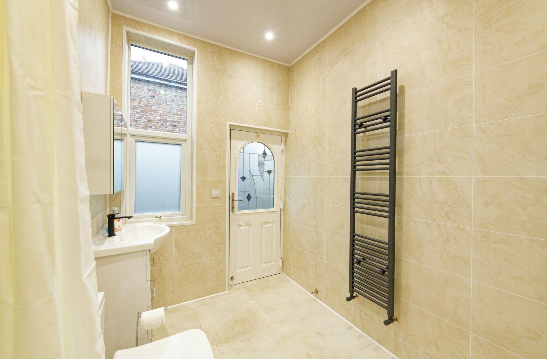 A bathroom with a bathtub, a sink, a towel rack, and a window with a view of a brick building.