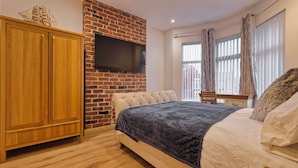 A bedroom with a brick fireplace, a bed with a dark blanket, a wooden wardrobe, and a TV mounted on the wall. - 4-BR Liverpool House Free Parking (Liverpool)