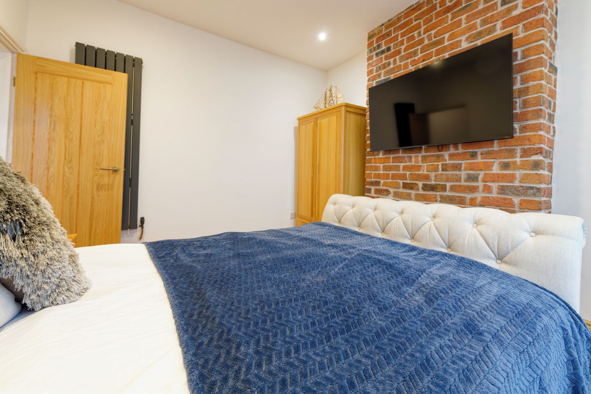 Une chambre à coucher avec un lit, une armoire en bois, un téléviseur fixé à un mur en briques et un radiateur.