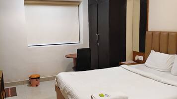 A hotel room with a bed, a wardrobe, a desk, a chair, and an air conditioning unit.