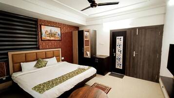 A hotel room with a bed, a ceiling fan, a desk, and a wardrobe.