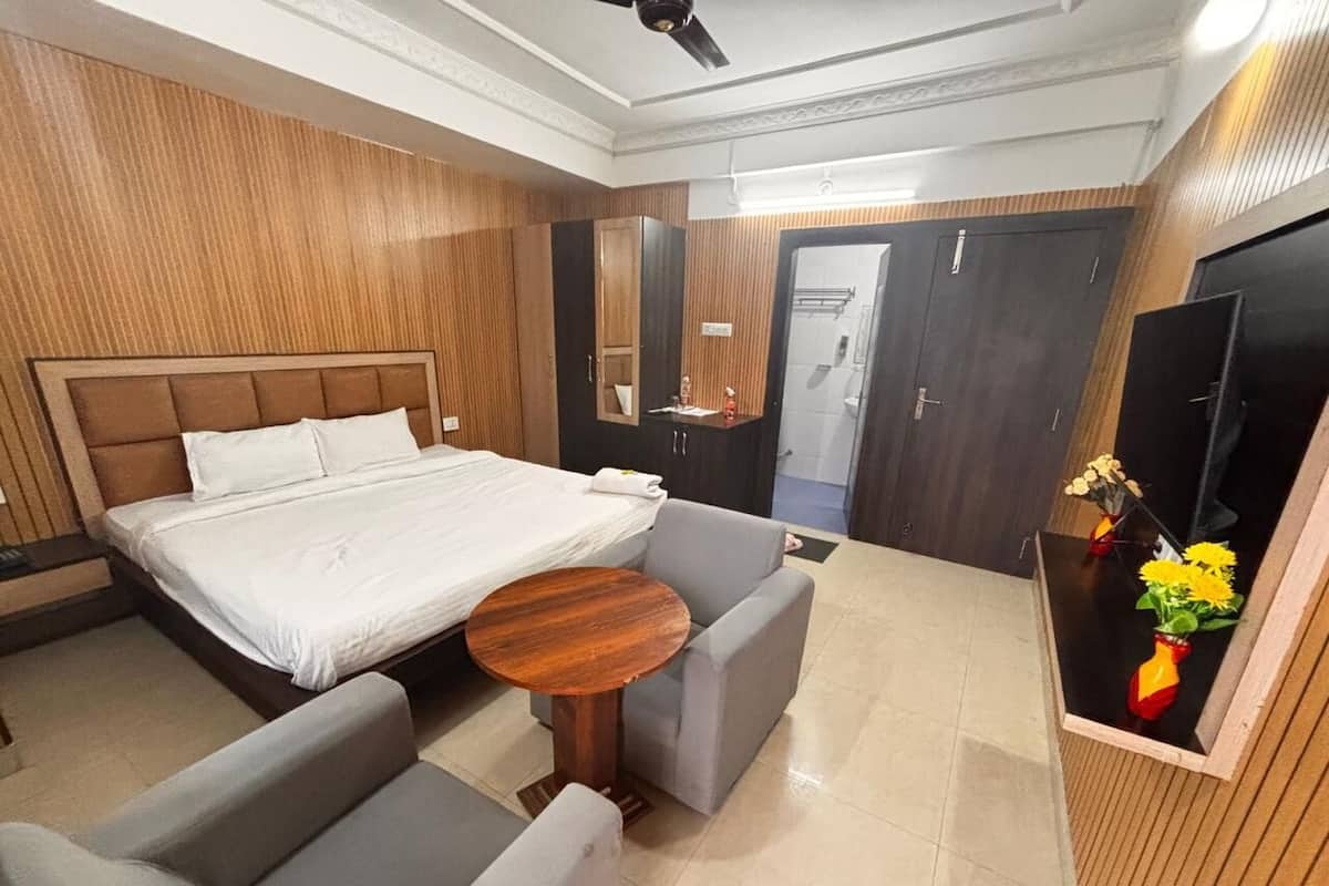 Habitación de hotel con cama, sofá gris, una mesita de madera y televisión.