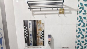 Ένα μπάνιο με λευκό νιπτήρα, έναν καθρέφτη διακοσμημένο με πλακάκια, μια κρεμάστρα για πετσέτες και μια περιοχή με ντους, με μπλε πλακάκια.