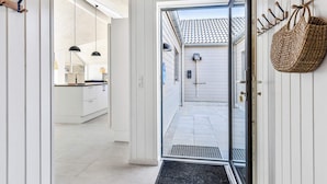 Corredor que dá para uma cozinha com telhado cerâmico, cesto pendurado e porta com puxador.