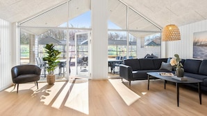 Quarto espaçoso com uma grande porta de vidro deslizante que dá para um pátio externo, um sofá escuro, uma mesa de centro e um lustre.
