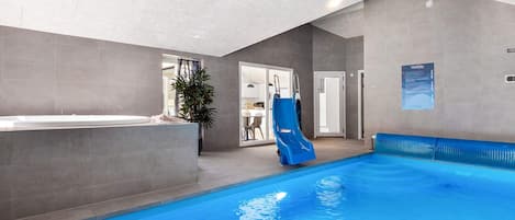 An indoor swimming pool with a slide, a reception area, and a door leading to a room.