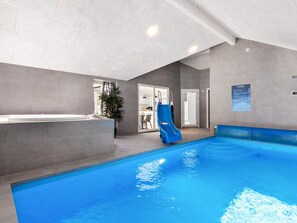 An indoor swimming pool with a slide, a reception area, and a door leading to a room.