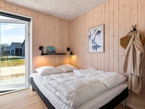 A bedroom with a bed, a window, a shelf with books, a wall art piece, and a coat rack.