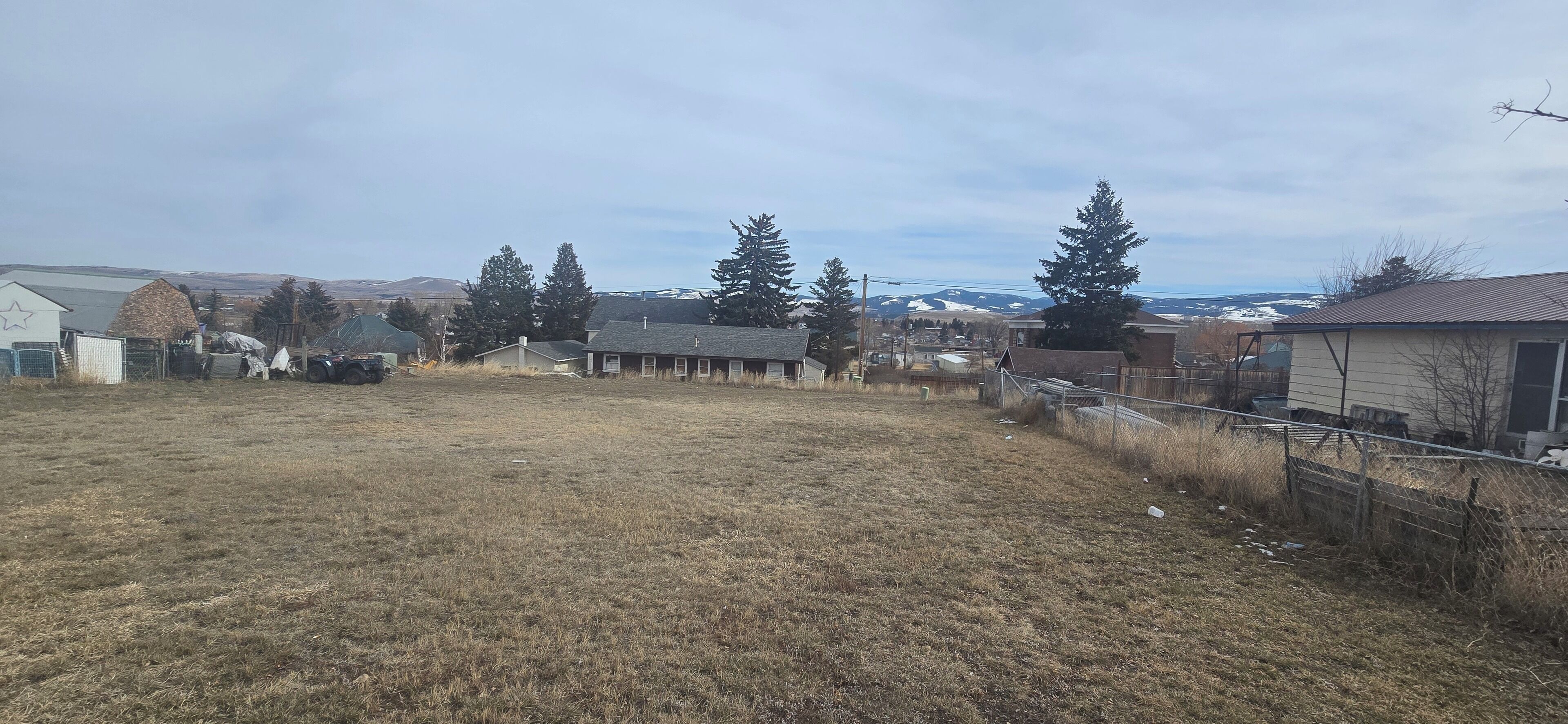 Un quartier résidentiel avec des maisons, une cour clôturée et une chaîne de montagnes visible au loin.