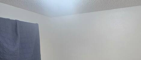 Un dormitorio con una cama de madera, una mesita de noche, una cortina azul y una lámpara de techo.