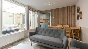 A modern living room with a grey sofa, a dining area with wicker chairs, and a kitchen in the background. - Spacious Duinland 188 Home With Veranda (Sint Maartensvlotbrug)