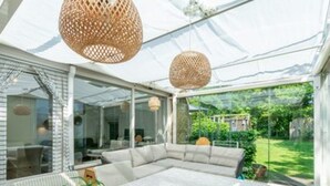 A modern outdoor living space with a sectional sofa, a dining table with a vase of flowers, and wicker pendant lights. - Spacious Duinland 188 Home With Veranda (Sint Maartensvlotbrug)