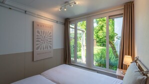 A hotel room with a bed, a window with curtains, a wall-mounted artwork, and a lamp on a bedside table. - Spacious Duinland 188 Home With Veranda (Sint Maartensvlotbrug)