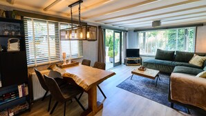 A modern living room with a wooden dining table, a sofa, and a TV. - Cozy forest cottage - cozy wooden cottage in the middle of nature on the Veluwe (Putten)