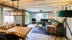 A modern living room with a wooden ceiling, a sofa, a coffee table, and a dining table. - Cozy forest cottage - cozy wooden cottage in the middle of nature on the Veluwe (Putten)