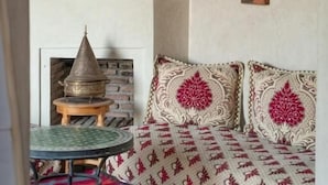 Et værelse med et traditionelt marokkansk design, med en mønstret sofa, et hængende messinginstrument og et lille bord med metalbordplade.