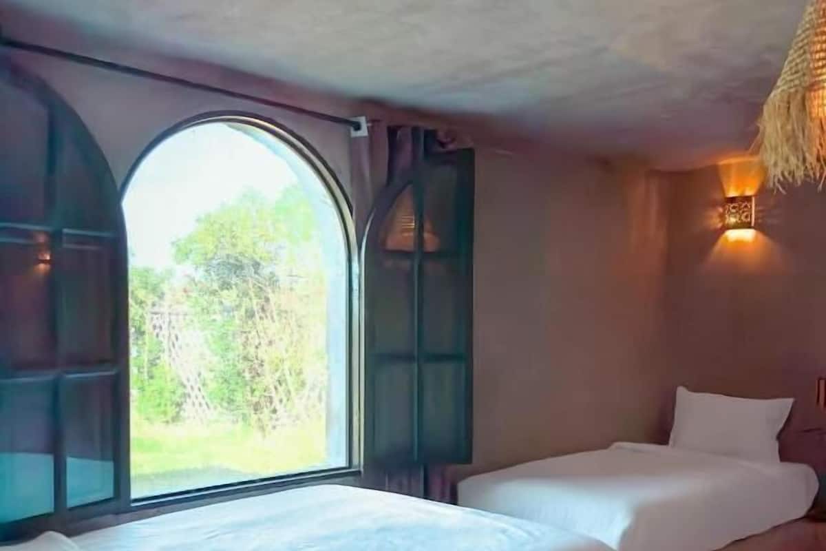 A room with two beds, a large window, and a hanging light fixture.