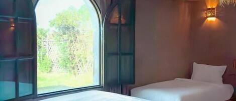 Une chambre avec deux lits, une grande fenêtre et un luminaire suspendu.