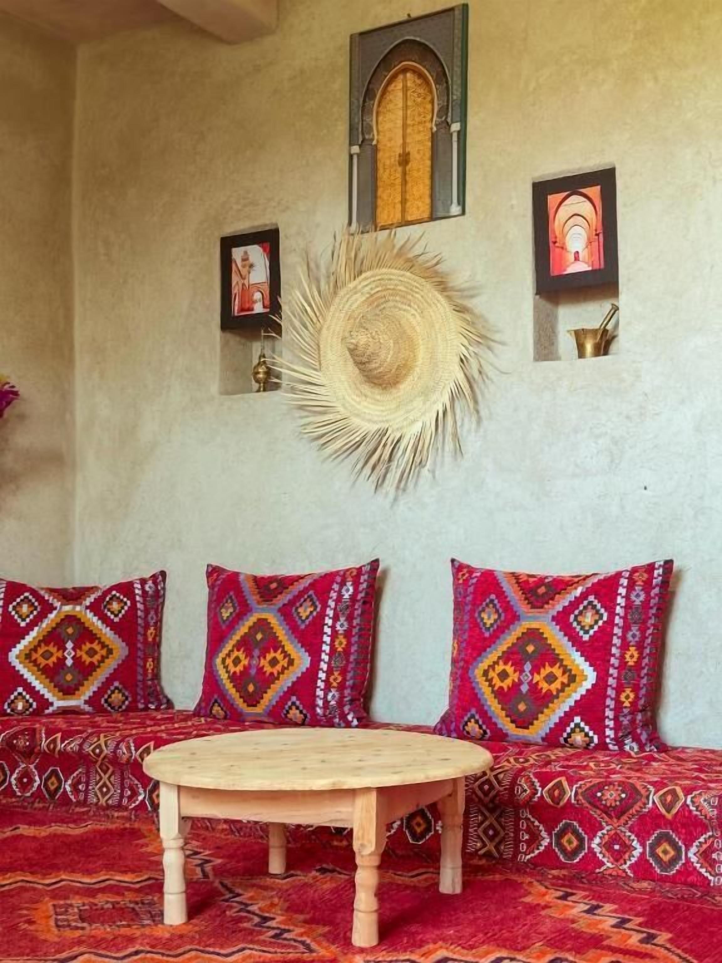 Une pièce avec une table ronde en bois, deux canapés à motifs, une décoration murale et une petite fenêtre en arc de cercle.