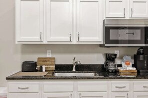 A kitchen with white cabinets, a stainless steel sink, a microwave, a toaster, and a coffee maker. - The Pete Rose Suite | A Cozy Modern Brick Home (Louisville)