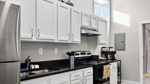 A modern kitchen with white cabinets, stainless steel appliances, and a black countertop. - Legends Retreat: A spacious stay for large groups (Louisville)