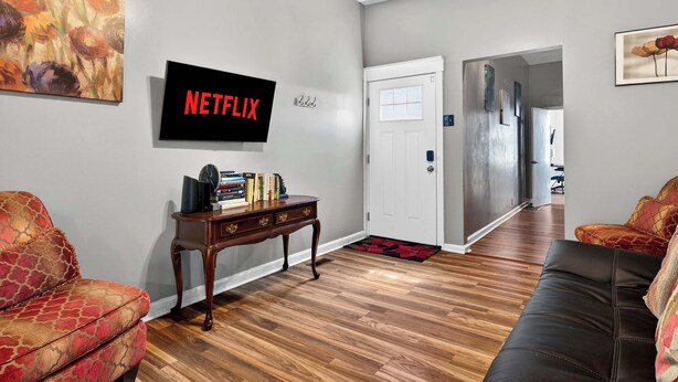 Una sala de estar con un televisor de pantalla plana, una mesa de centro, un sofá y una puerta que da a otra habitación.