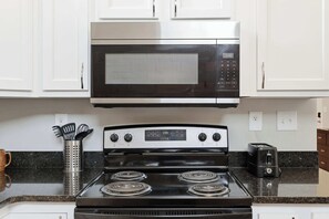 A kitchen with white cabinets, a stainless steel microwave, a stove with four burners, and a toaster. - The Booker Noe Suite | Brick Home w/ Modern Design (Louisville)