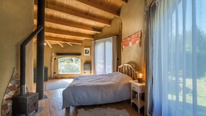 Een slaapkamer met een groot bed, een houten plafond, een open haard en uitzicht op de omgeving.