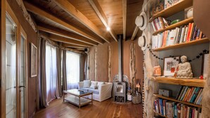 Een gezellige woonkamer met een witte bank, houten vloeren, een open haard en een boekenkast vol boeken.